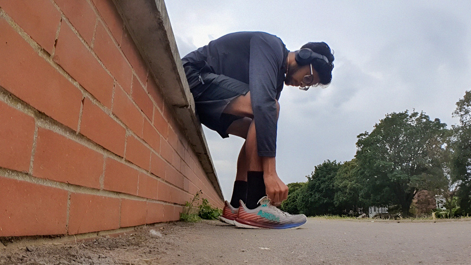 A person crouching by a brick wall, adjusting their running shoe laces.